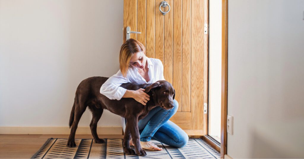 young woman sitting with dog inside the front door to their home